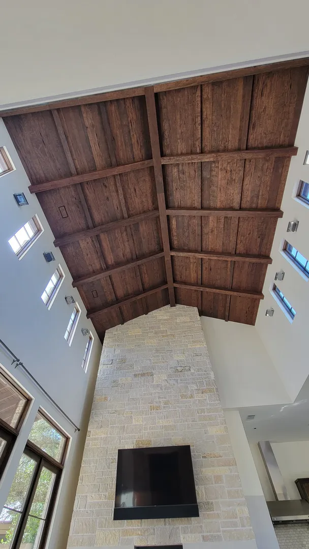 Tall room view showing the vaulted wood ceiling aligned over a full-height stone fireplace.