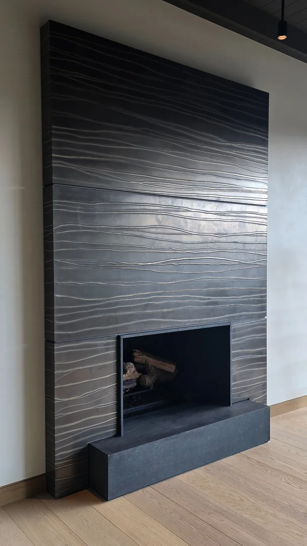 Dark fireplace surround with flowing horizontal lines, a rectangular firebox and a raised hearth.