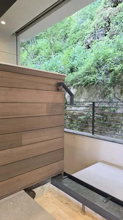 Wood-clad exterior stair landing with black steel railings opening toward a densely planted hillside.