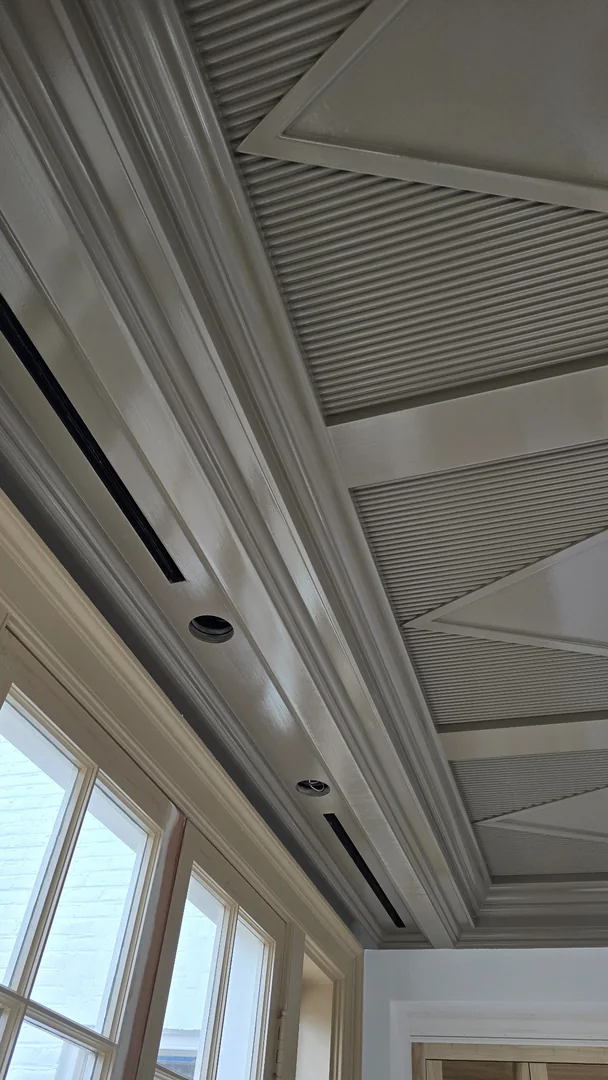 Painted ceiling with ribbed panels, geometric trim, crown molding and recessed light openings above tall windows.