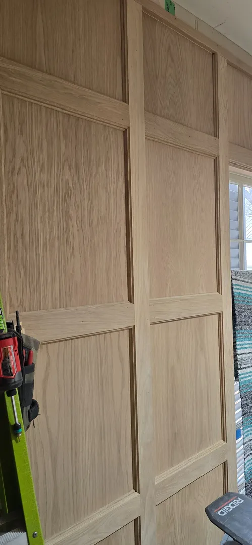 Full-height white oak wall paneling and integrated doorway during finish installation.