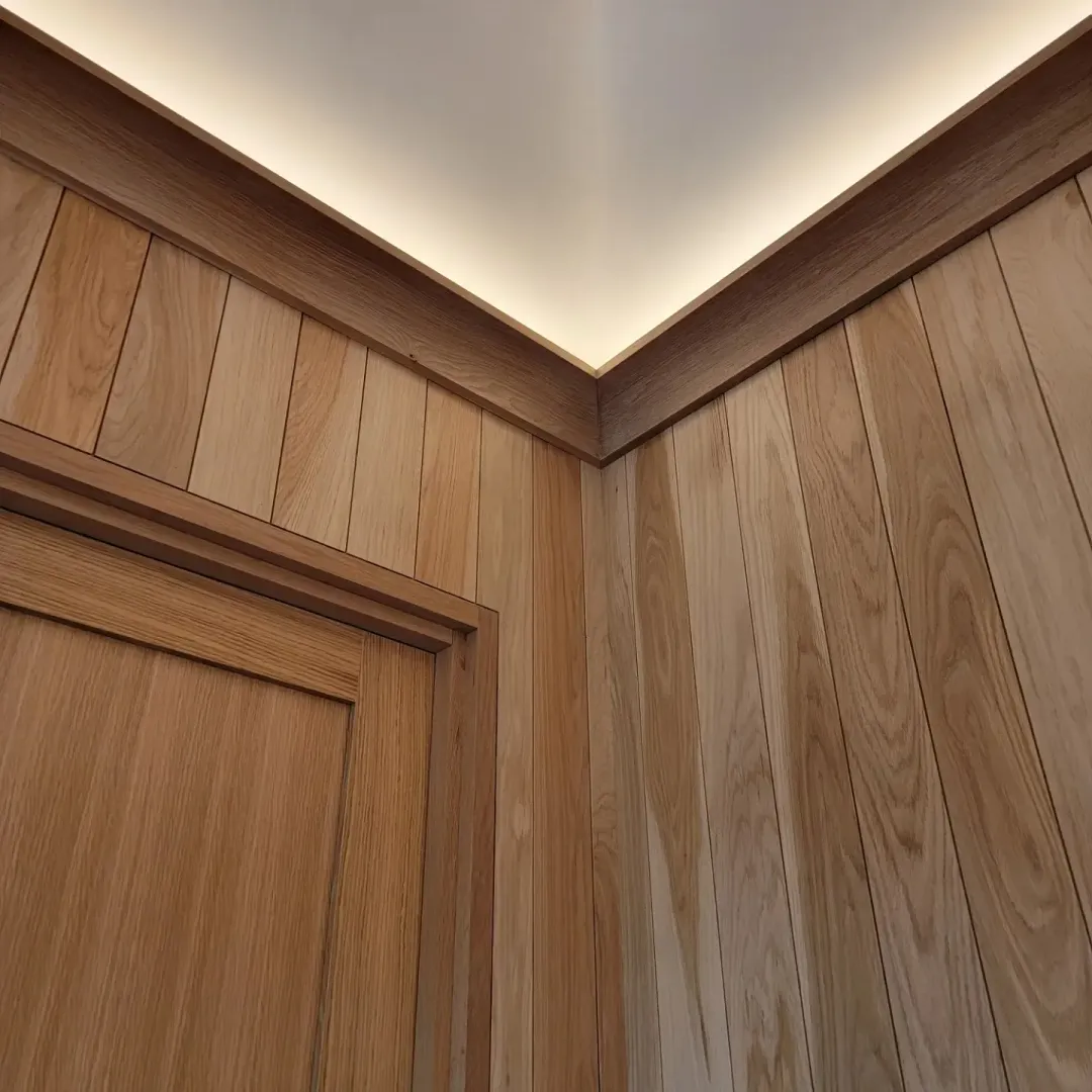 Close view of oak wall paneling, door casing, and illuminated ceiling cove.