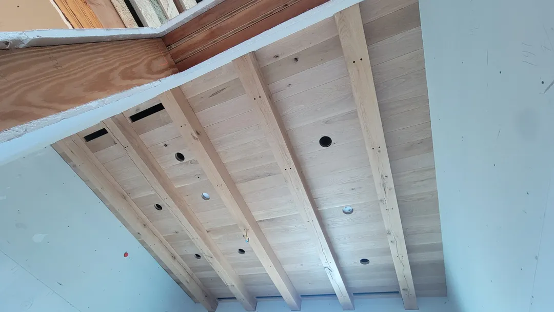 Paneled wood ceiling framed by finished beams above an arched room opening.