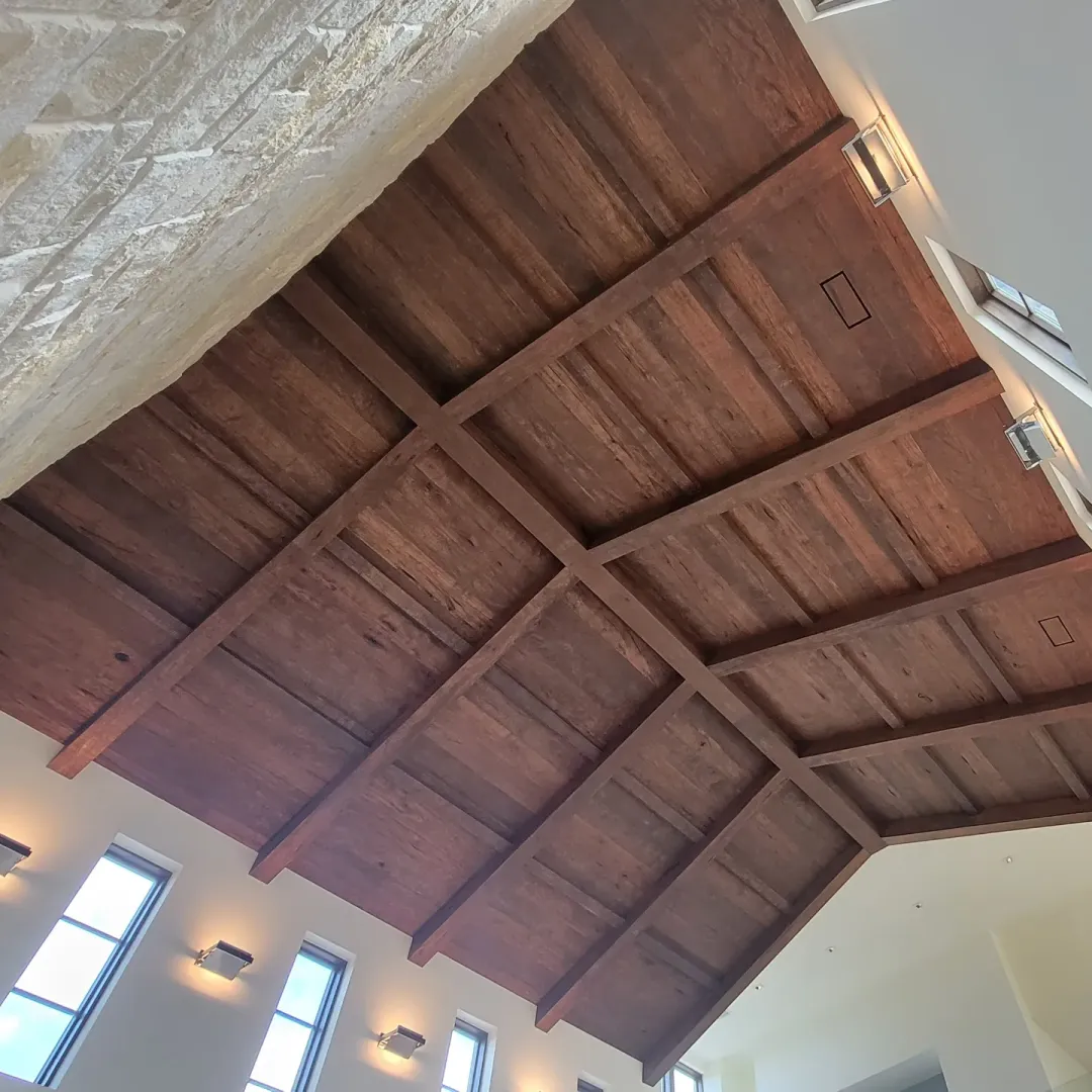 Completed vaulted wood ceiling with aligned beams, paneled bays, integrated lighting, and a tall stone fireplace wall.