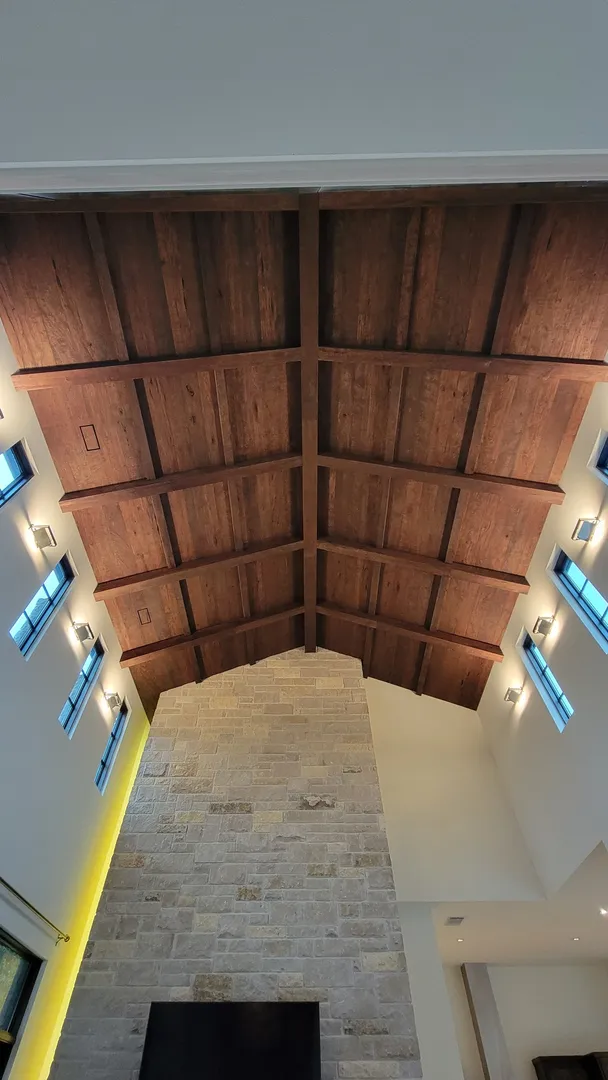 Vaulted wood ceiling nearing completion above the stone fireplace and high clerestory windows.